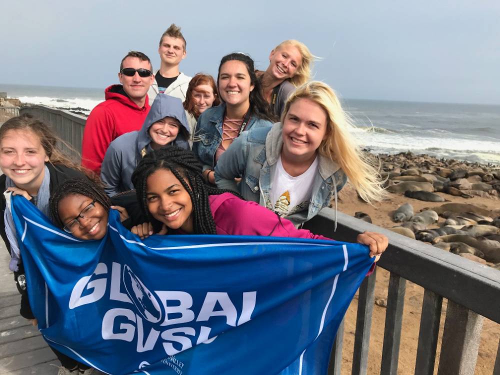 Students holding a GVSU flag by the ocean